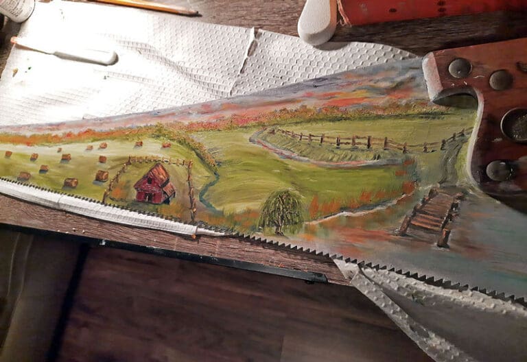 Painting of a barn and fields on an old saw blade. painted by Claire Lee