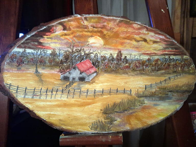 Painting of a barn and fields with trees in the background on a slice of a tree trunk